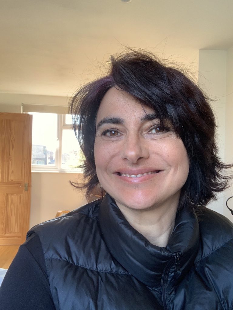 A photograph of Dr Emily Salines. A white woman with black hair and a black top. Emily is smiling a the camera.