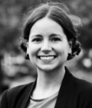Black and white photograph of Laura da Costa with dark hair and a a black jacket, smiling.